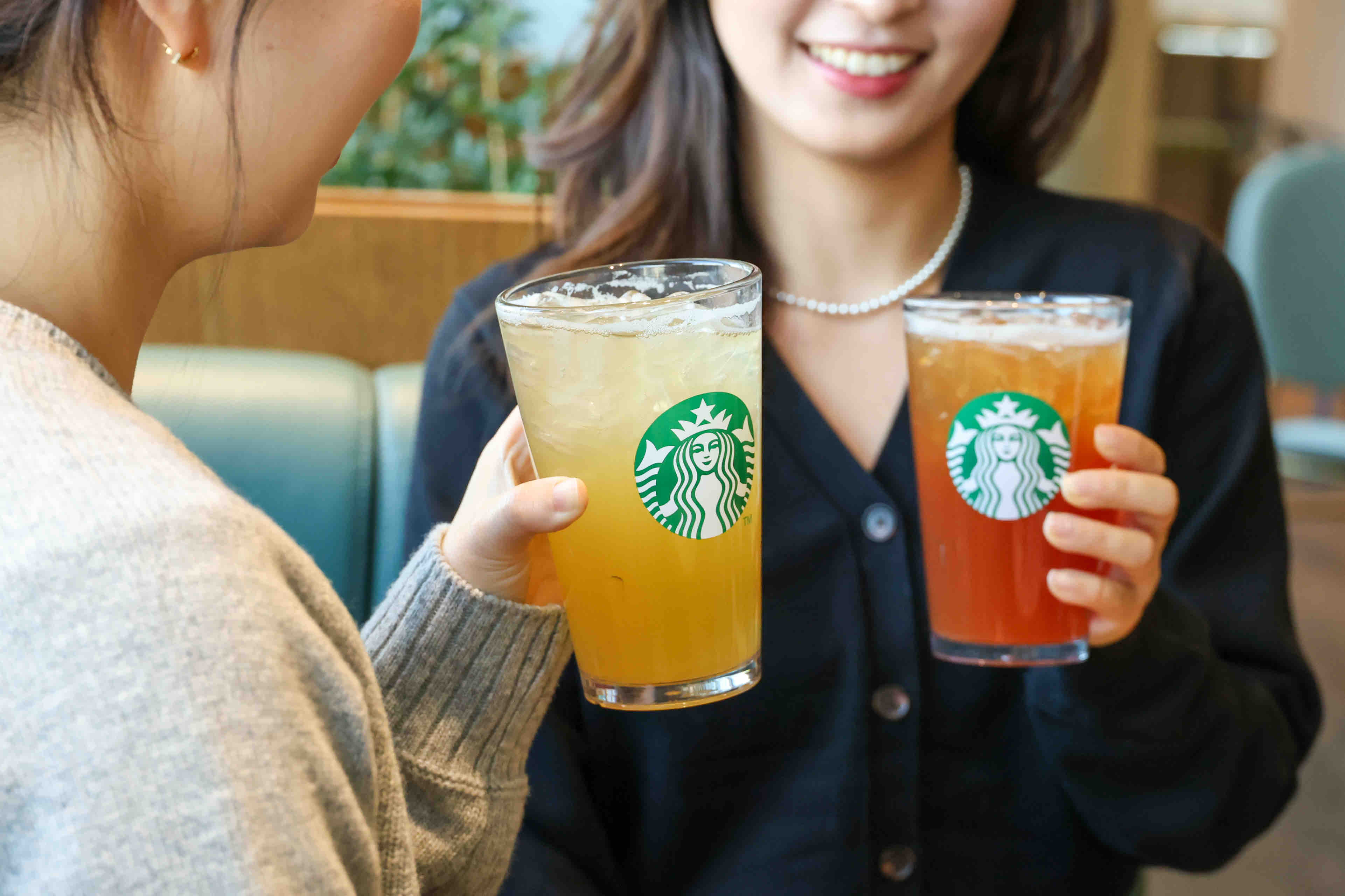 스타벅스 매장에서 아이스 차 음료를 들고 즐겁게 대화하고 있는 두 여성의 모습