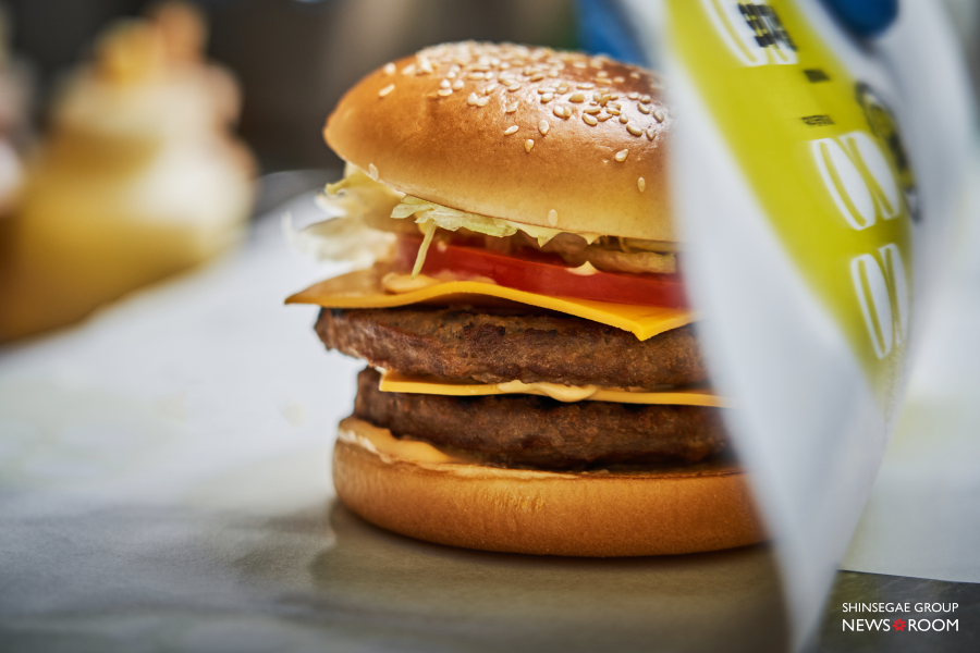 노브랜드 버거 주방에서 집게로 직화 패티를 들어 올려 햄버거를 조리하고 있는 신선한 현장 모습